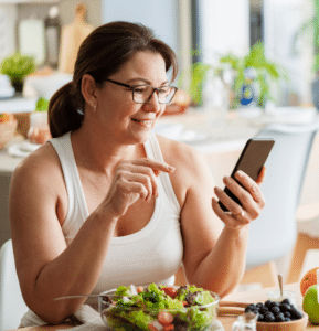 A woman looks at her phone at the kitchen table, reviewing her medically-supervised weight loss plan